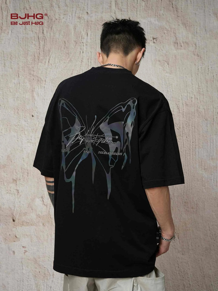Black reflective butterfly print t-shirt worn by a model showing back design in casual street style.