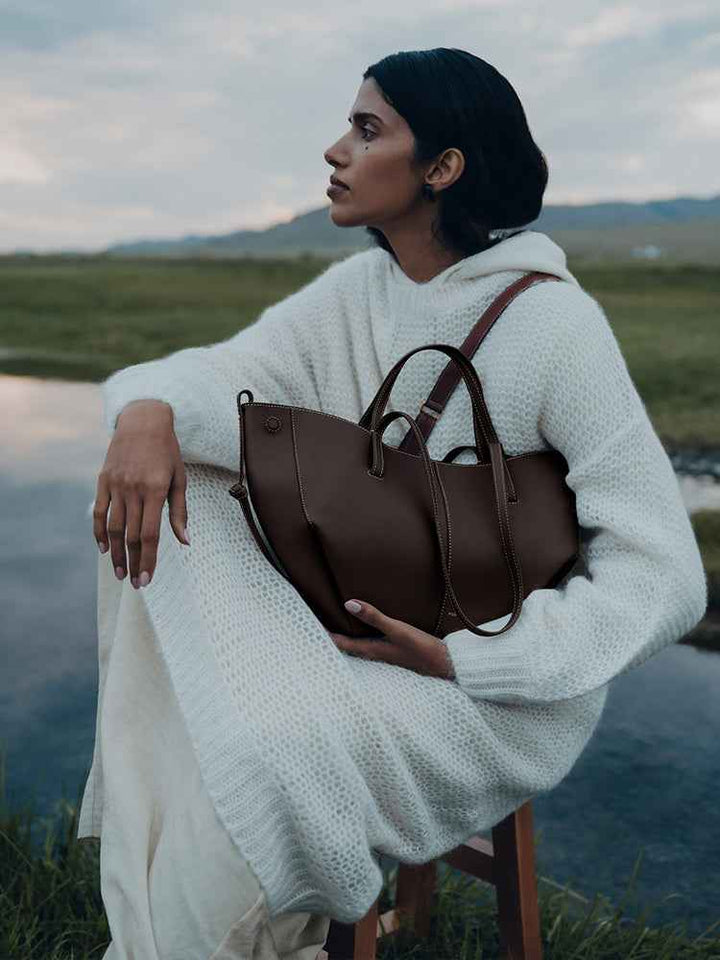 Woman wearing white knit sweater dress holding maroon Polène Cyme Mini leather tote bag outdoors