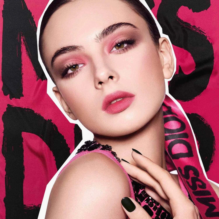 Close-up of a woman wearing Dior Miss Dior Fall 2025 makeup with pink eyeshadow and lipstick against a vibrant pink background with Dior branding.