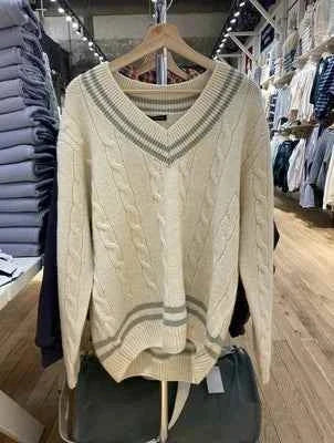 Classic winter sweater with cable knit design and striped edges in off-white color hanging in a clothing store.