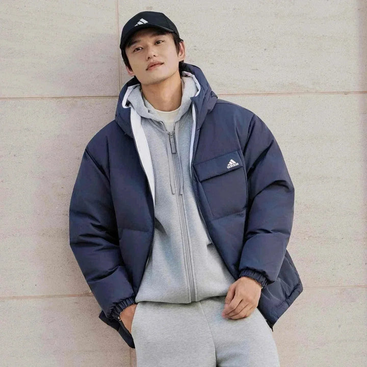 رجل يرتدي Adidas جاكيت 600 Puff كحلي دافئ وكاجوال مع غطاء رأس وشعار أديداس على الصدر
