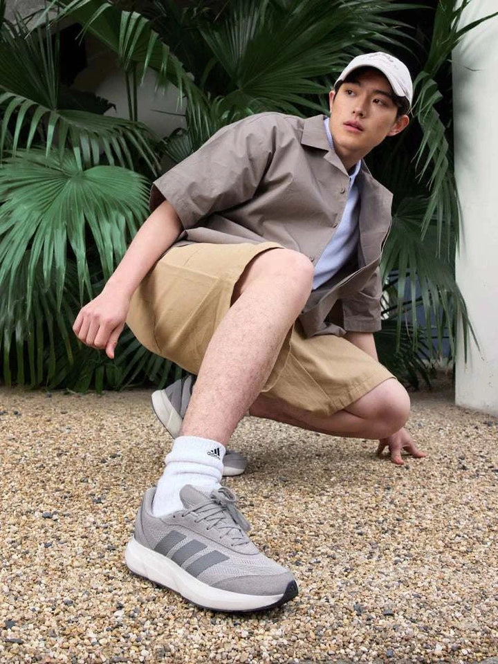 رجل يرتدي أحذية Adidas رمادية للجري والاستخدام اليومي مع جوارب بيضاء وقبعة بيضاء في مكان خارجي طبيعي