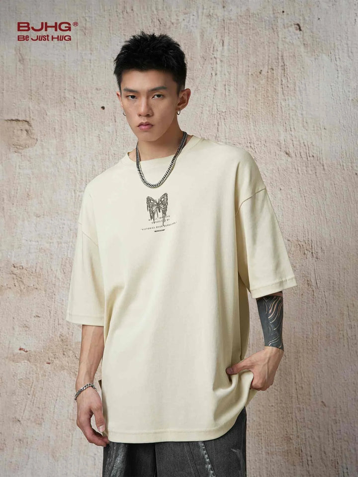 Young man wearing beige reflective butterfly print T-shirt with casual street style against textured wall