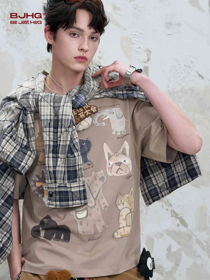 Casual beige T-shirt with playful cartoon animal prints worn by a young man with a plaid shirt draped over shoulders.