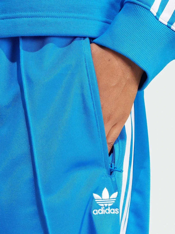 Close-up of bright blue Adidas sports pants with white stripes and zippered side pocket showing Adidas logo