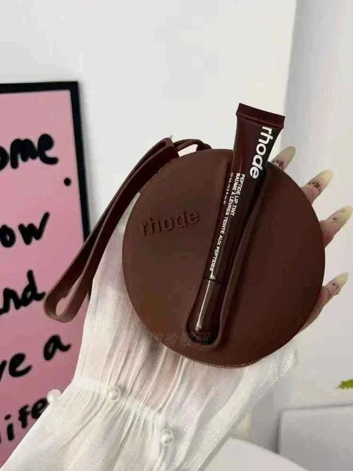 Rhode Peptide Lip Tint in warm brown shade with matching round silicone pouch for elegant lip hydration and color.