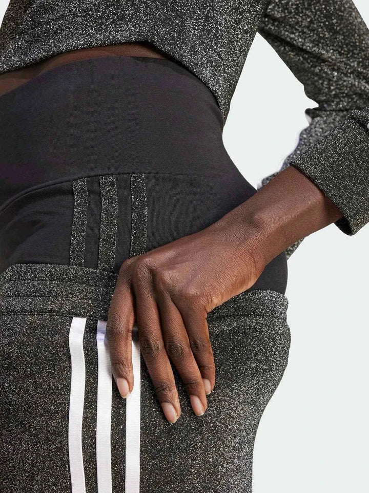 Close-up of shiny Adidas pants with classic three stripes design, worn with a matching top.