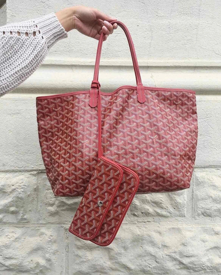 red geometric patterned hobo bag حقيبة كتف with leather strap and matching pouch held against stone wall background