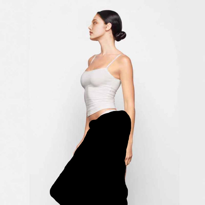 Woman wearing SKIMS توب بحمالات رفيعة essential cami top in a soft, fitted design against white background