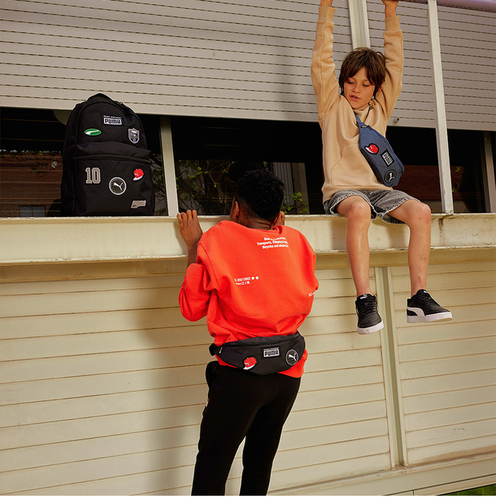 black Puma backpack with patches on a ledge and two kids wearing casual sporty outfits and Puma bags outdoors