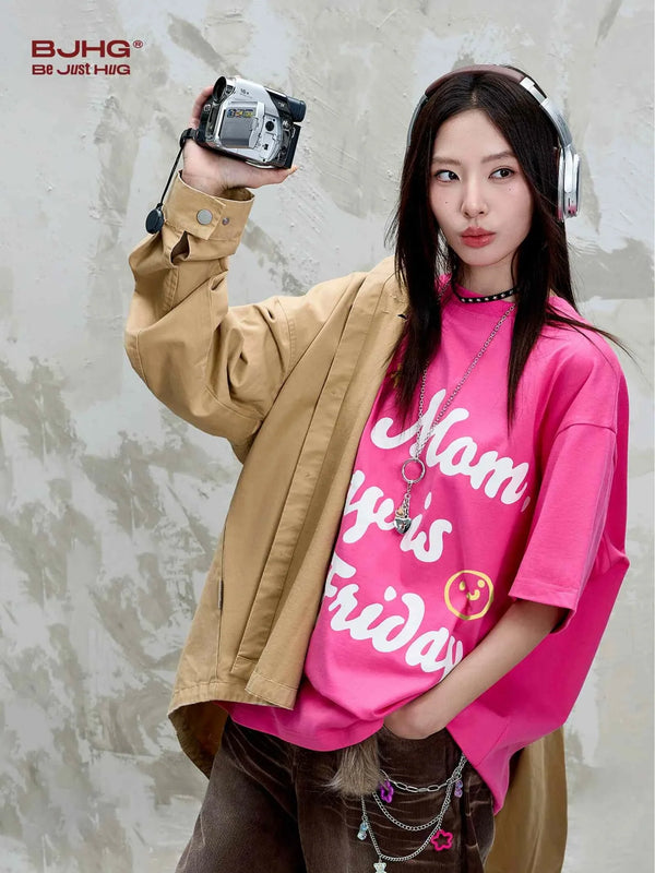 Young woman wearing pink تيشيرت مطبوع بشعار Mom Day is Friday with casual beige jacket and headphones.
