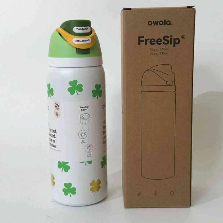 Owala Thermos CupKitty Limited Edition stainless steel insulated water bottle with green clover design and leak-proof FreeSip lid next to its cardboard packaging