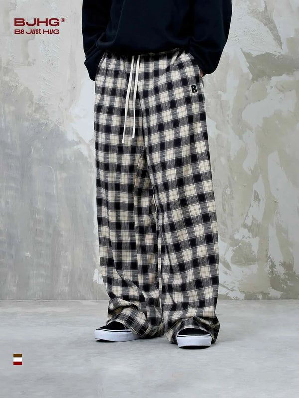 wide checkered pants BJHG with loose fit and classic plaid pattern in black and white on model wearing black top and sneakers against textured gray wall