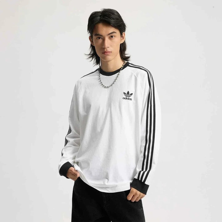 رجل يرتدي تيشيرت قطني adidas أبيض بأكمام طويلة مع خطوط سوداء وشعار Trefoil