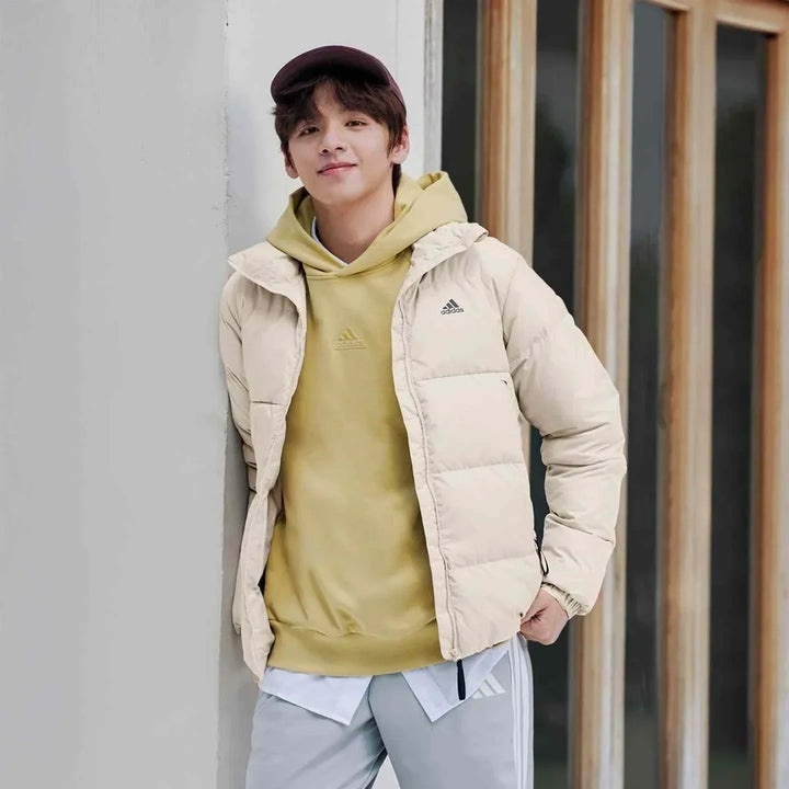 رجل يرتدي Adidas جاكيت داون مبطن بلون بيج مع هودي أصفر وقبعة كاجوال في مشهد حضري