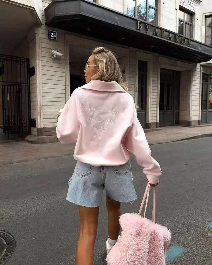 امرأة ترتدي سويت شيرت وردي ناعم بأكمام واسعة وياقة قابلة للطي مع شورت جينز وتحمل حقيبة وردية ناعمة في شارع المدينة