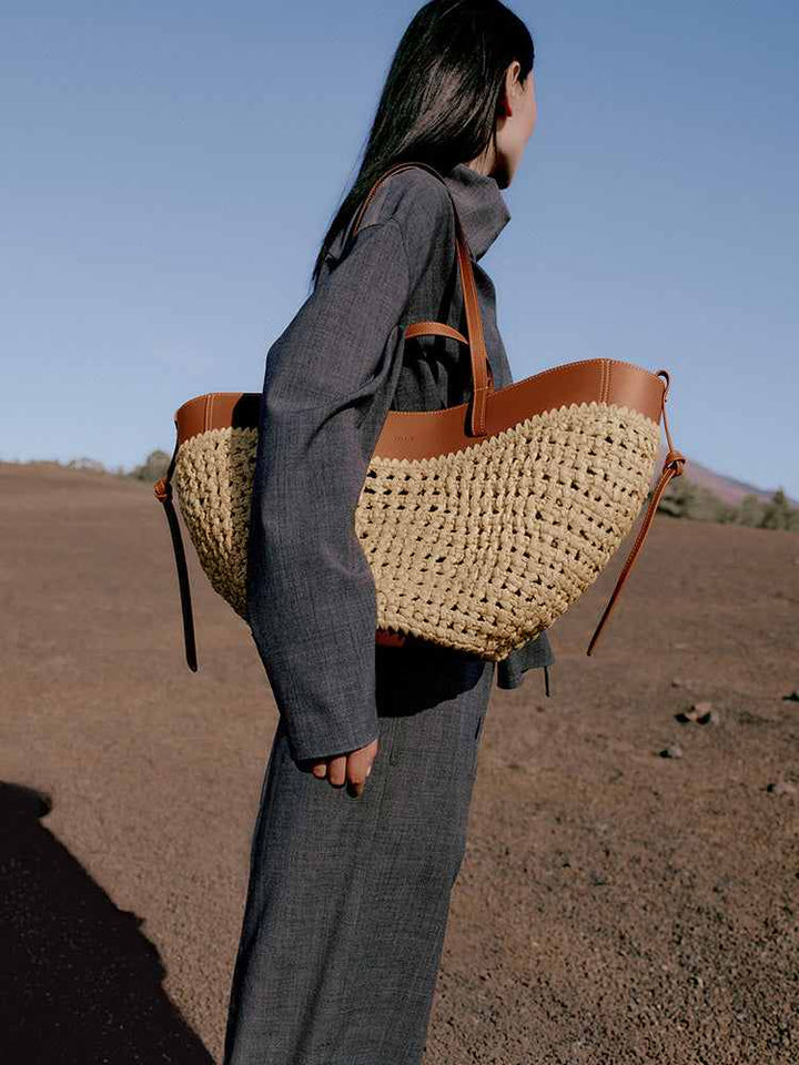 Polène Cyme raffia tote bag with cowhide leather details and adjustable shoulder strap carried by woman outdoors