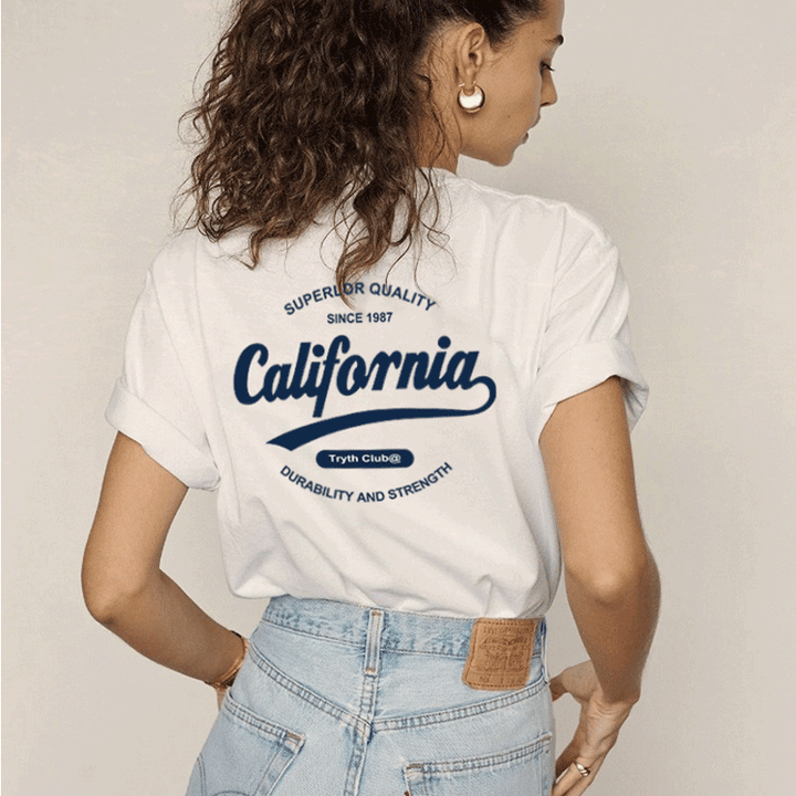 Woman wearing white California Club casual cotton t-shirt with rolled sleeves and blue print on the back paired with light blue high-waisted jeans.