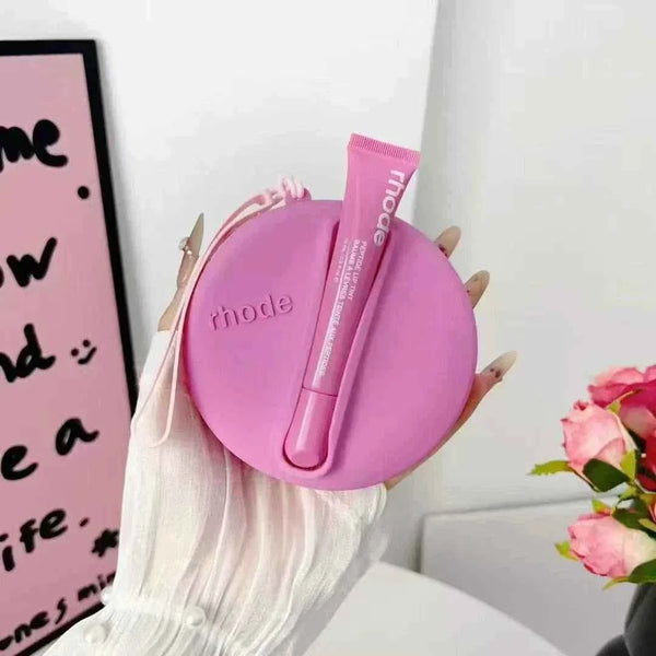 Rhode Peptide Lip Tint in pink tube with matching round silicone pouch held by hand with white sleeve and pink flowers nearby