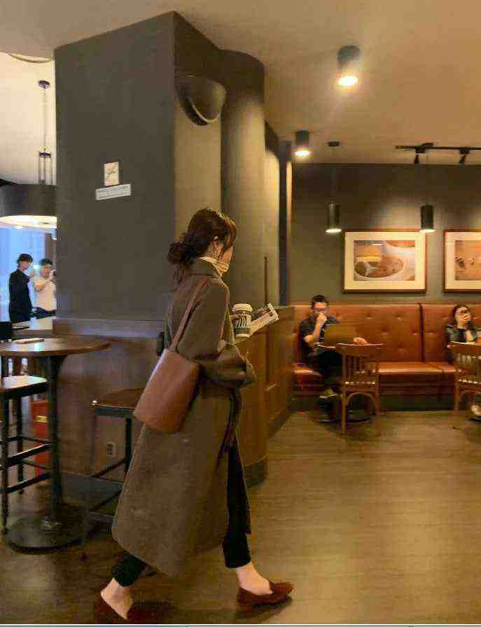 luxurious long winter coat made from premium goat wool in dark brown worn by woman in indoor cafe setting