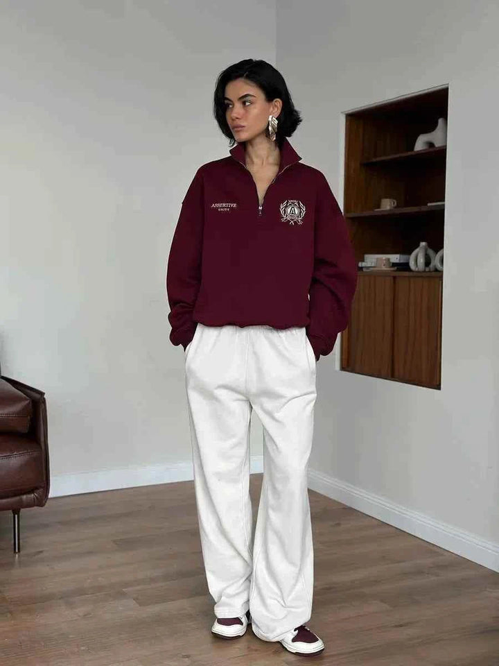 سويت شيرت فضفاض أوروبي وأمريكي برقبة نصف سحاب باللون العنابي مع بنطلون أبيض واسع داخل غرفة حديثة