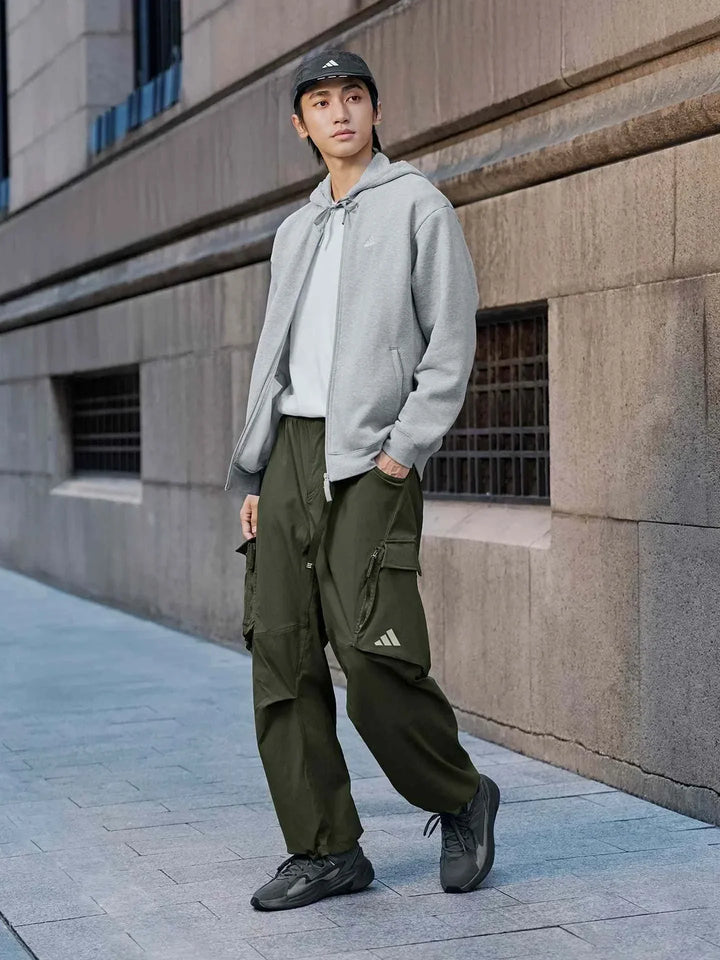 رجل يرتدي Adidas | أديداس جاكيت واسع رمادي مع بنطال أخضر وحذاء رياضي أسود في شارع حضري