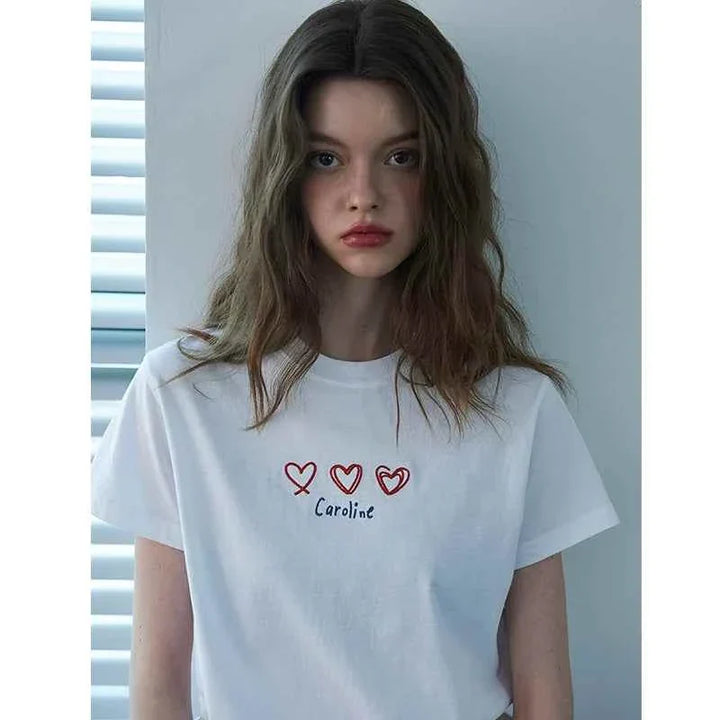 White Caroline Hearts t-shirt with embroidered red hearts and handwritten "Caroline" text worn by a woman