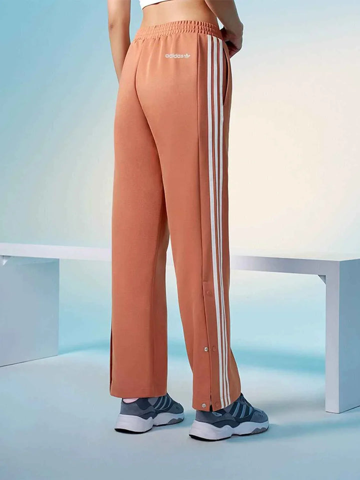 Adidas wide-leg sports pants in peach with classic three stripes and elastic waistband for comfort