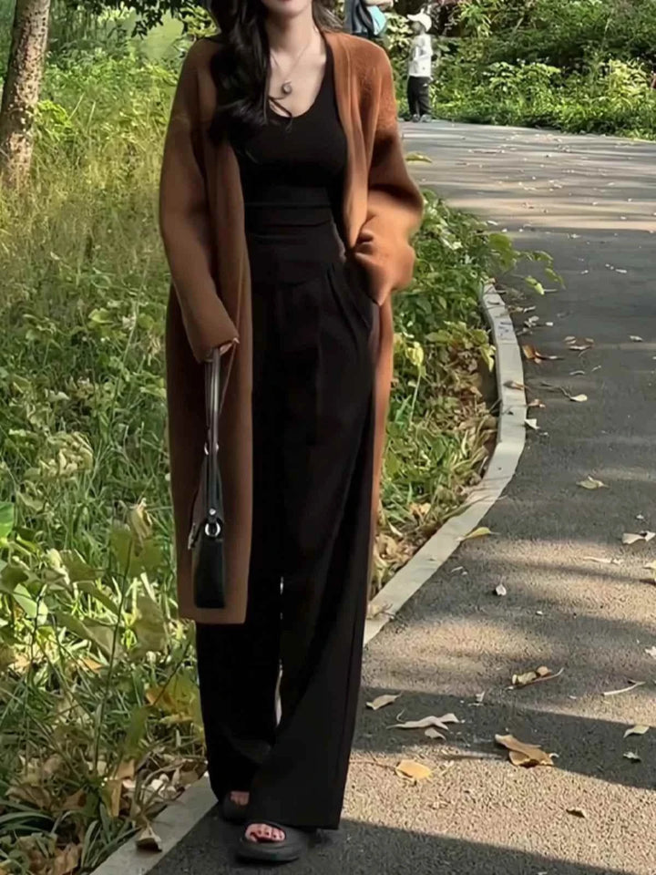 woman wearing dark brown long wide winter cardigan with black outfit walking outdoors in park pathway