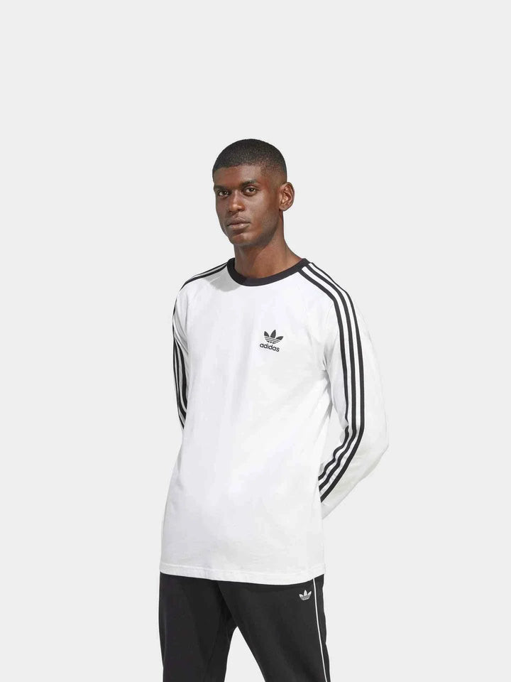 رجل يرتدي adidas تيشيرت قطني أبيض بأكمام طويلة مع خطوط سوداء وشعار Trefoil