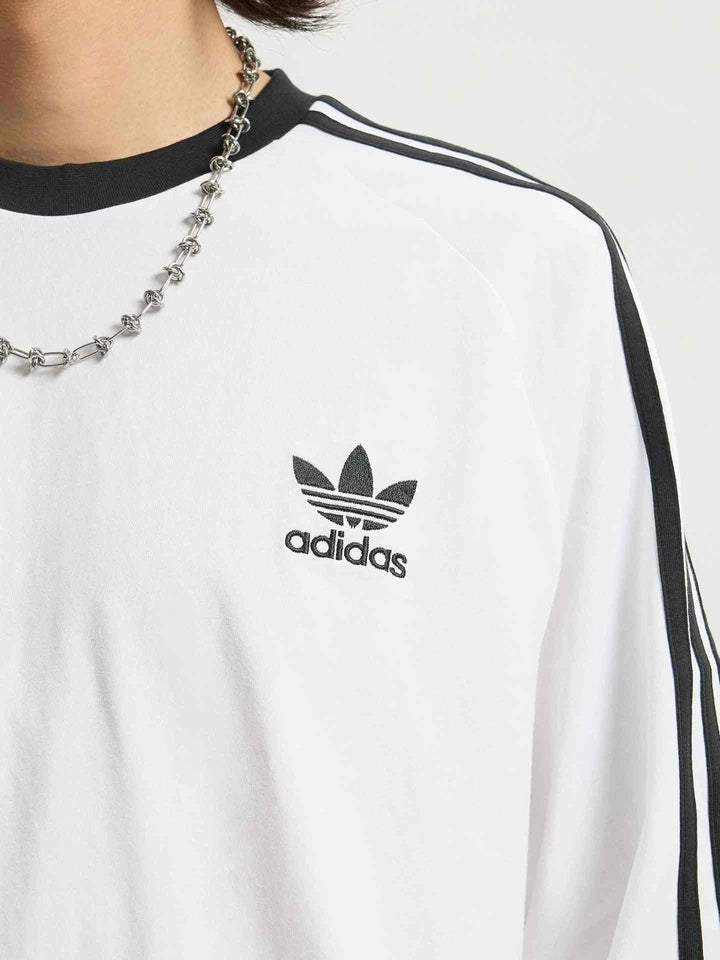 adidas تيشيرت قطني أبيض بأكمام طويلة مع خطوط سوداء وشعار Trefoil مطرز