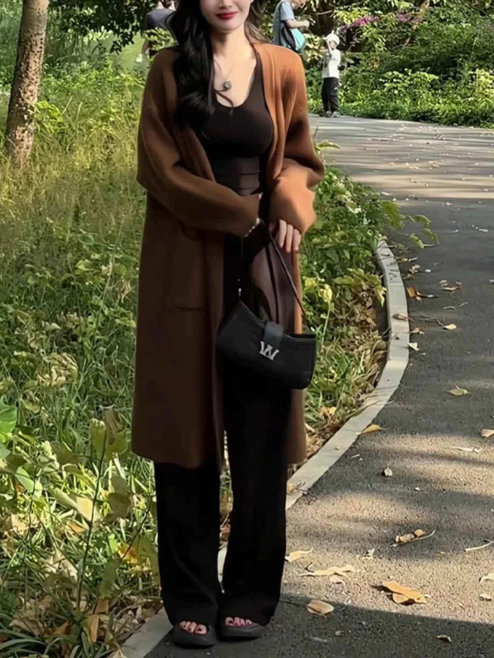 كاردجان شتوي طويل بني داكن واسع يرتديه امرأة في الهواء الطلق مع بنطال أسود وحقيبة صغيرة