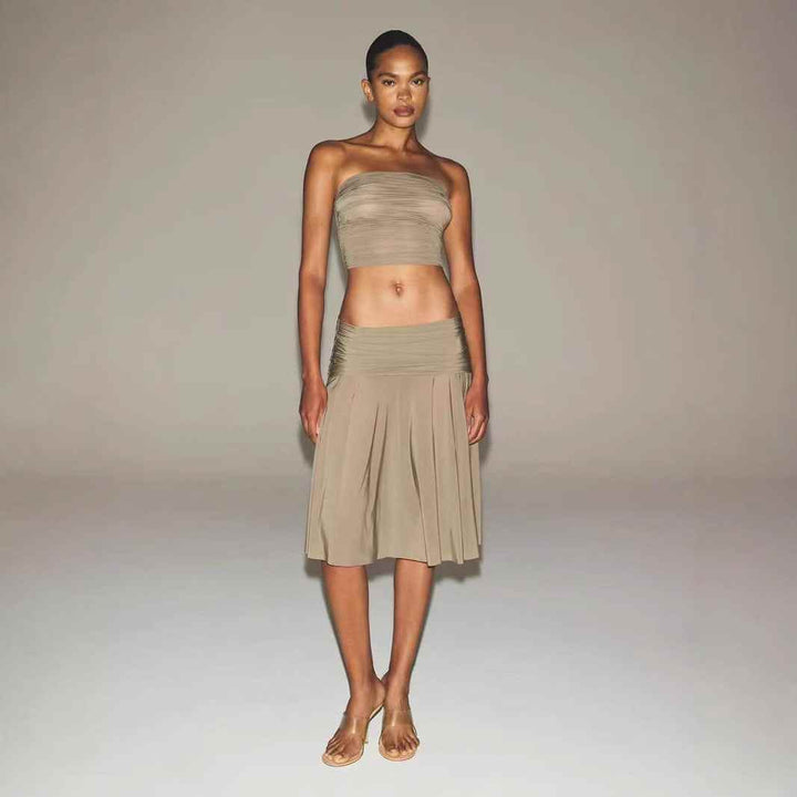 Elegant ruched bandeau crop top by SKIMS in soft beige tone modeled with matching pleated skirt