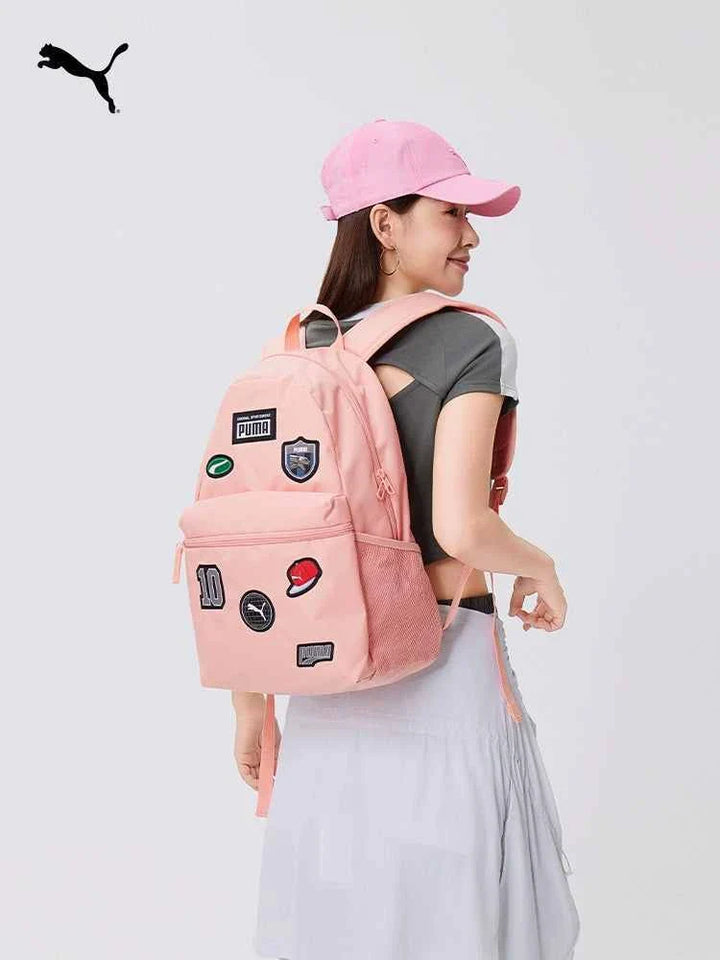 Woman wearing a pink PUMA backpack with multiple patches, adjustable padded straps, and mesh side pockets, styled for casual and school use.