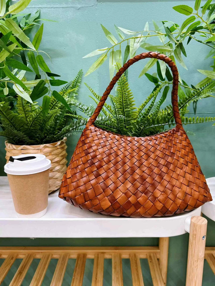 brown dragon woven bag made of braided natural leather with a comfortable handle on a white table next to a coffee cup and green plants in the background