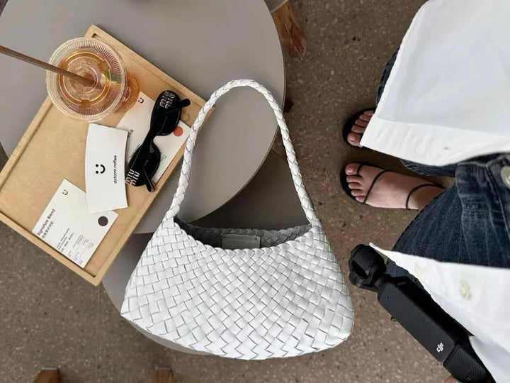 white dragon woven bag made of natural cow leather with braided design on a gray table next to sunglasses and a drink