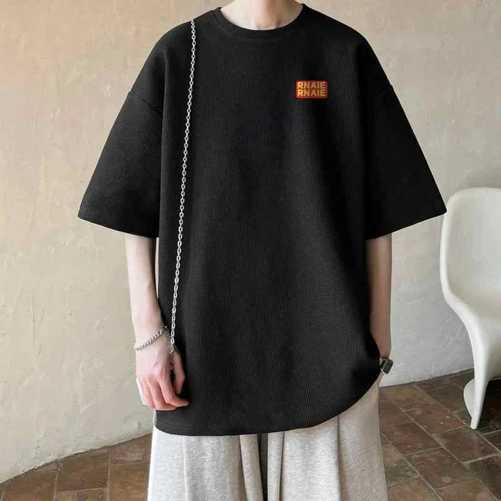 black oversized MORRYING t-shirt with cartoon character print worn by person with light gray pants and silver chain accessory