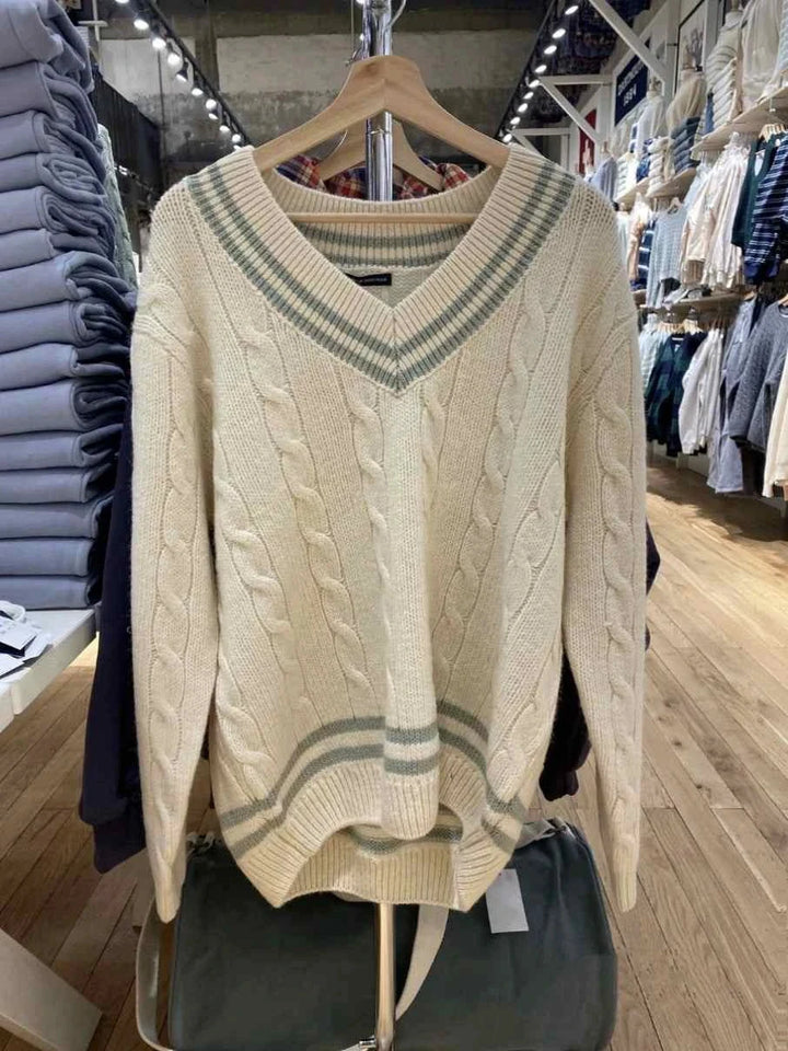 classic cable knit winter sweater with striped edges in off-white color hanging in a store