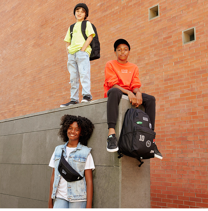 group of young people wearing stylish casual outfits with black PUMA backpacks and fanny pack, urban brick wall background, showcasing practical and trendy حقيبة الظهر backpacks for school and daily use