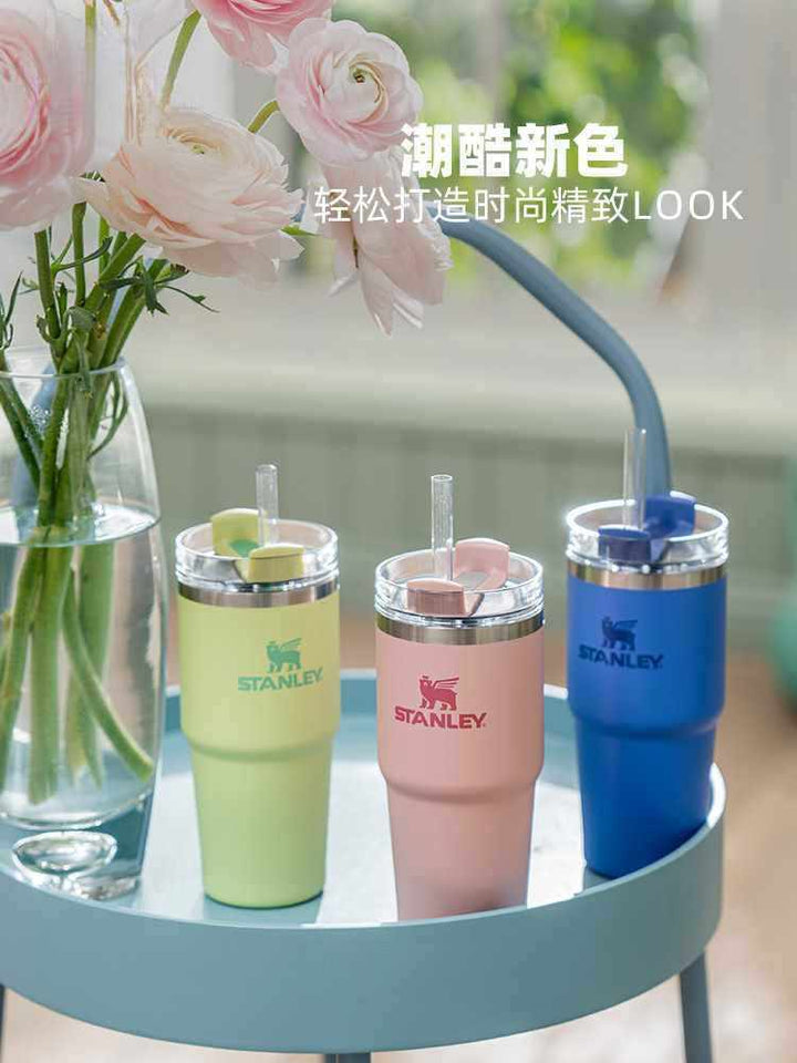 Three Stanley Quencher H2.0 cups in pastel colors on a table with flowers in the background.