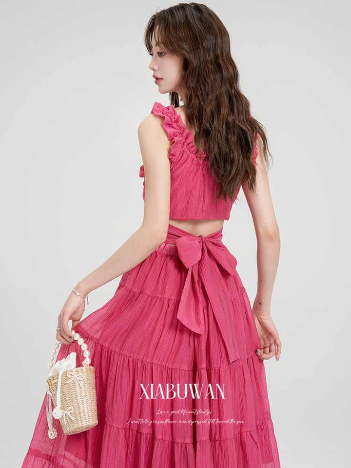 Woman in a pink open-back suspender dress carrying a woven beach bag, perfect for a women's summer seaside resort.