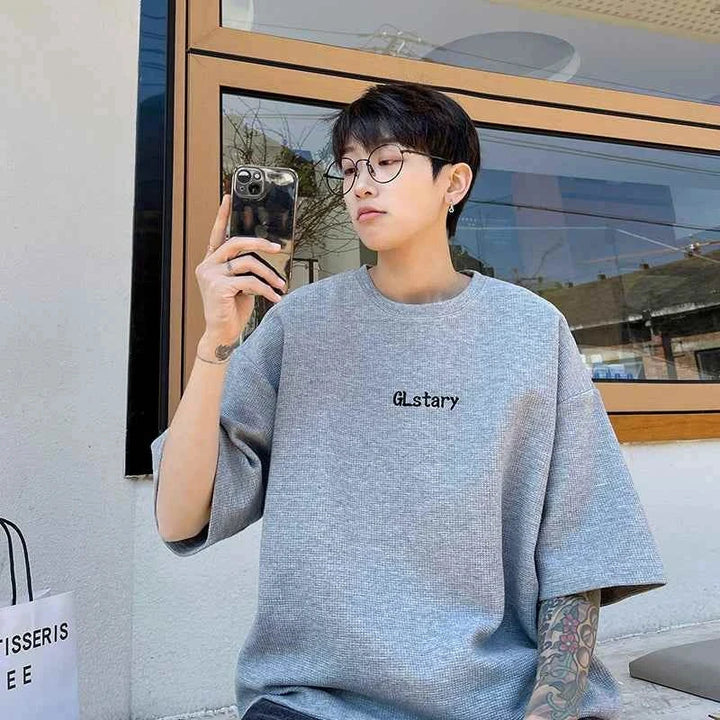 Gray loose fit MORRYING T-shirt with cartoon character print worn by young man taking selfie outdoors