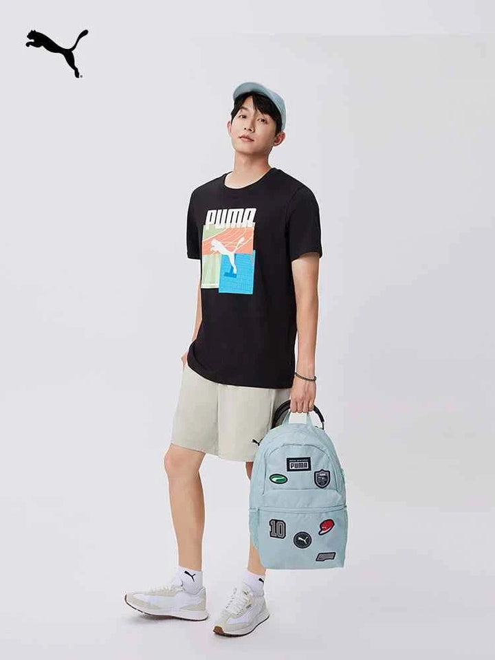 young man holding light blue PUMA backpack with patches and zippers, casual sporty outfit