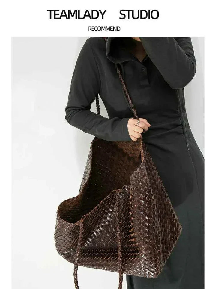 Large handmade woven dark brown genuine leather tote bag with shoulder strap held by woman in black dress