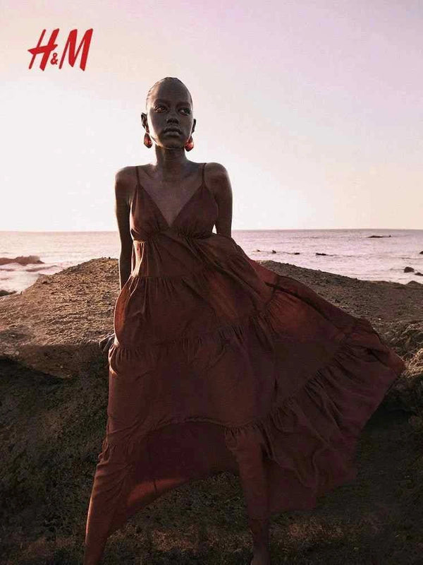 H&M brown tiered maxi dress with deep V-neck and adjustable straps, worn by model on beach.