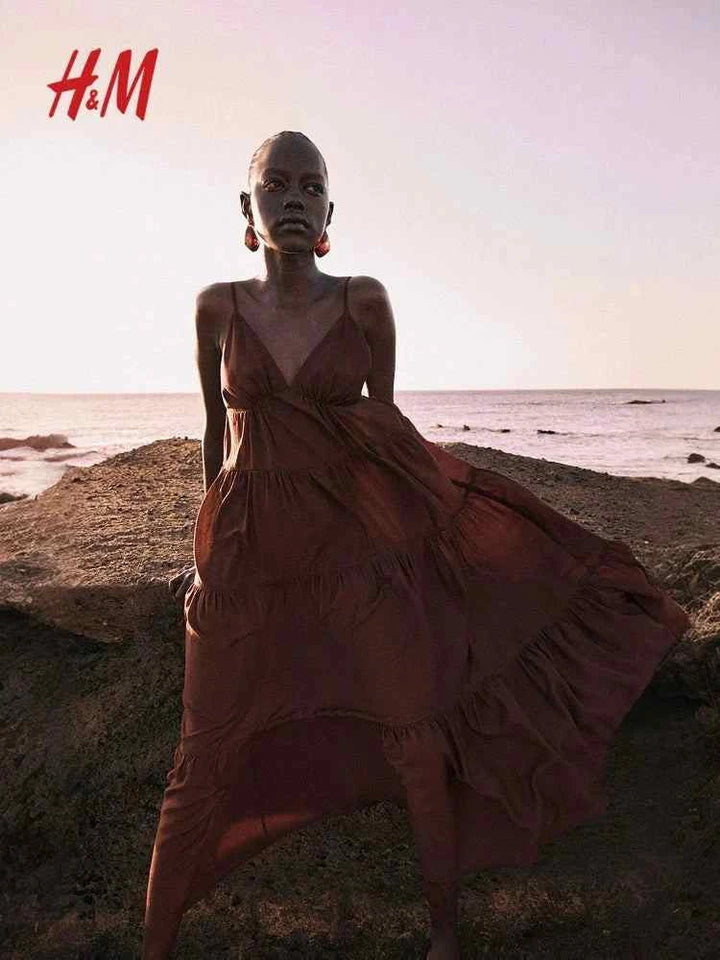 H&M brown tiered maxi dress with deep V-neck and adjustable straps, worn by model on beach.