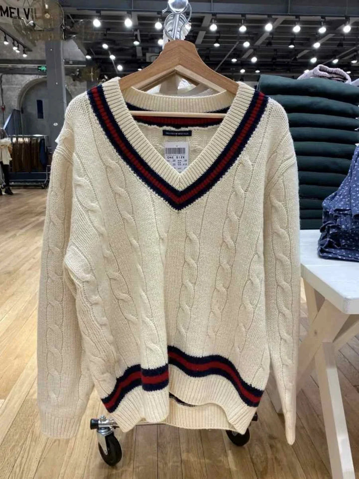classic cable knit winter sweater with striped edges in off-white color displayed on a hanger in a store