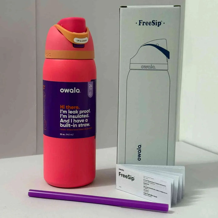 Owala FreeSip insulated pink stainless steel water bottle with leak-proof lid and built-in straw next to packaging and user manual