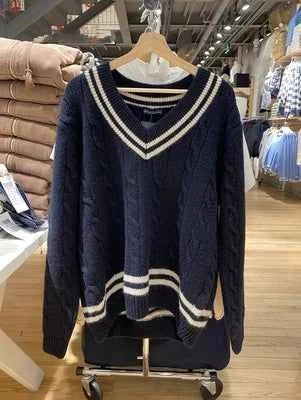 Classic winter sweater with cable knit design and striped edges in navy blue and white hanging in store