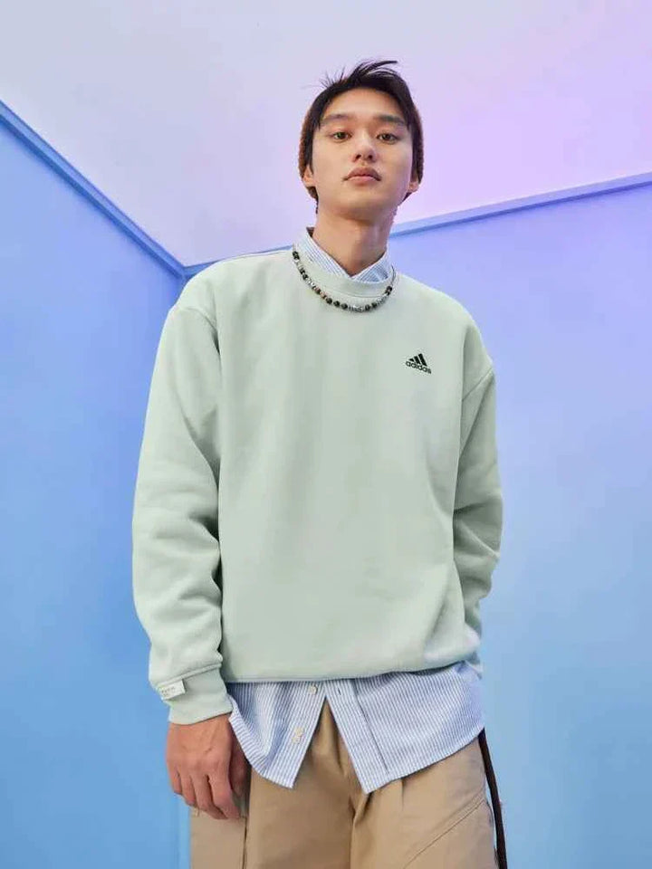 رجل يرتدي سويت شيرت Adidas | أديداس أخضر نعناعي بأكمام طويلة وشعار صغير على الصدر في خلفية زرقاء حديثة